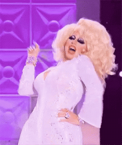 A Drag Queen Is Wearing A White Dress And Dancing On A Stage . GIF