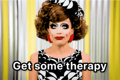 A Drag Queen Says " Get Some Therapy " In Front Of A Yellow Curtain GIF