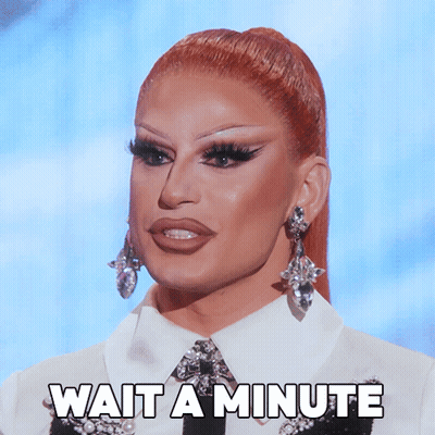 A Drag Queen Says Wait A Minute While Wearing Earrings And A White Shirt GIF