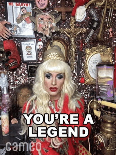 A Drag Queen Says " You 'Re A Legend " In Front Of A Wall Of Memorabilia GIF