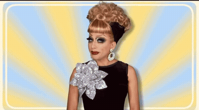 A Drag Queen Wearing A Wig And Earrings Is Smiling GIF