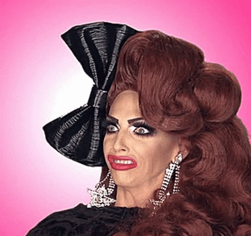 A Drag Queen With A Black Bow In Her Hair And Earrings GIF