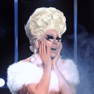 A Drag Queen With Blonde Hair And A White Fur Collar GIF
