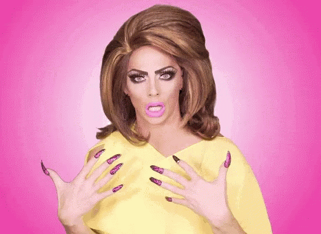 A Drag Queen With Long Purple Nails And A Yellow Top GIF