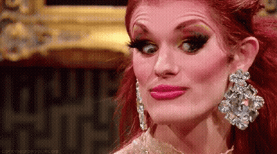 A Drag Queen With Red Hair And Earrings Is Making A Face . GIF