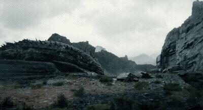 A Dragon Is Laying On The Ground In The Middle Of A Mountain GIF