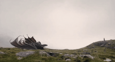 A Dragon Is Sitting On Top Of A Hill With Its Wings Spread GIF
