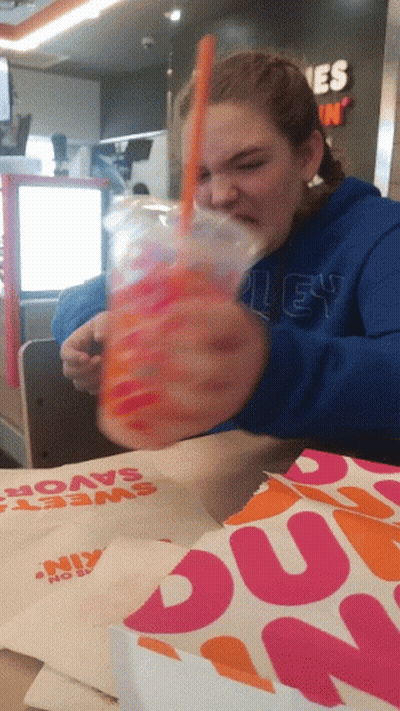 A Dunkin Donuts Bag Sits On The Table Next To A Girl GIF
