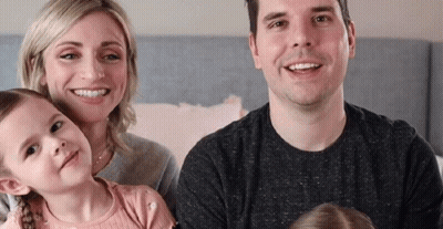 A Family Is Posing For A Picture While Sitting On A Bed And Smiling At The Camera . GIF