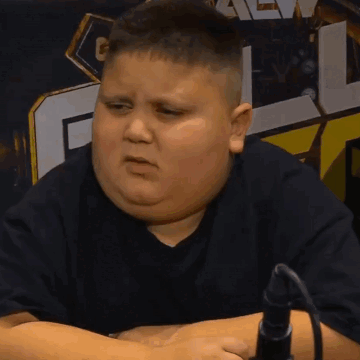 A Fat Boy In A Black Shirt Is Sitting In Front Of A Microphone And Making A Face GIF