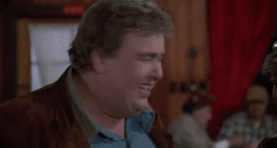 A Fat Man In A Blue Shirt And Brown Jacket Is Making A Funny Face . GIF