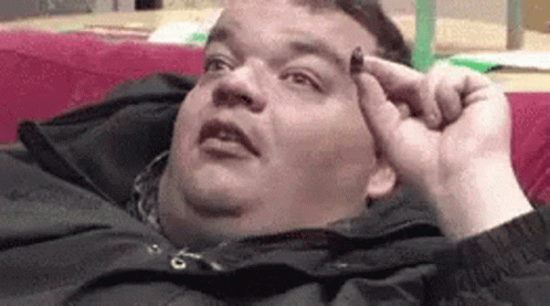 A Fat Man Is Laying On A Couch Holding Something To His Head . GIF