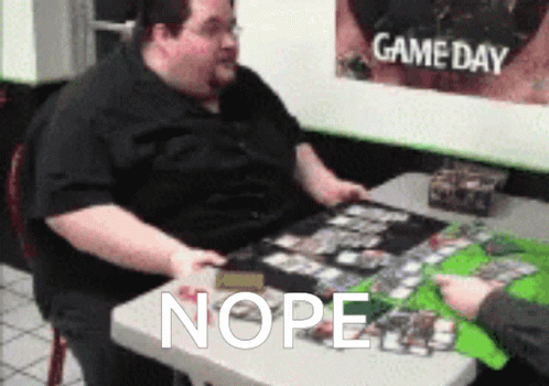 A Fat Man Sits At A Table With A Game Day Poster Behind Him GIF