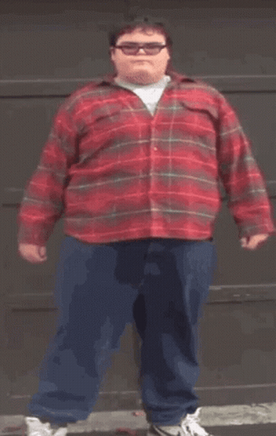 A Fat Man Wearing A Red Plaid Shirt And Blue Pants Is Standing In Front Of A Garage Door . GIF