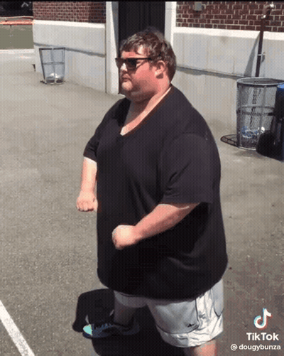 A Fat Man Wearing Sunglasses And A Black Shirt Is Standing In Front Of A Brick Building .. GIF