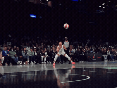 A Female Basketball Player Dribbles A Ball In Front Of A Crowd That Is Watching A Game GIF