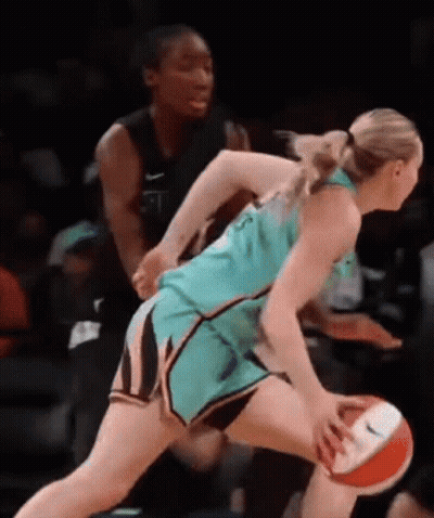 A Female Basketball Player Is Dribbling The Ball While Another Female Basketball Player Tries To Stop Her . GIF