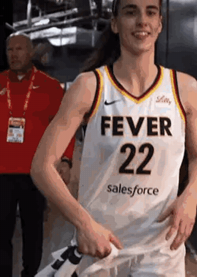 A Female Basketball Player Wearing A Fever 22 Jersey Is Standing In A Locker Room With Her Hands On Her Hips . GIF