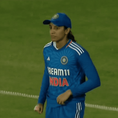 A Female Cricket Player Is Standing On A Field Holding Her Shirt . GIF