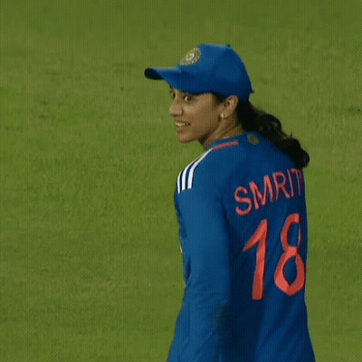A Female Cricket Player Wearing A Blue Jersey And A Hat Is Walking On A Field . GIF