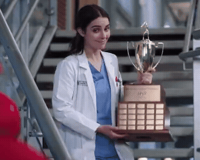A Female Doctor In A Lab Coat Is Holding A Trophy . GIF