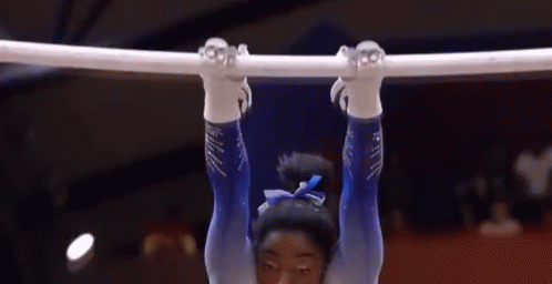 A Female Gymnast Is Hanging Upside Down On A Bar In A Gym . GIF