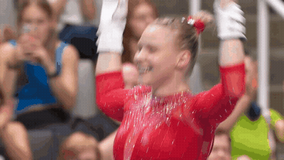A Female Gymnast Is Raising Her Arms In The Air In Front Of A Crowd . GIF