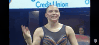 a female gymnast is waving her hand in front of a sign that says credit union