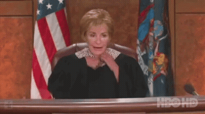 A Female Judge Is Sitting At A Desk In Front Of An American Flag In A Courtroom . GIF