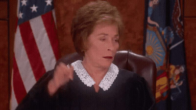 A Female Judge Is Sitting In Front Of An American Flag And Scratching Her Head . GIF