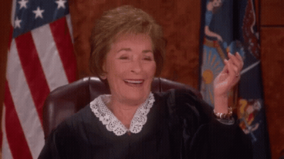A Female Judge Is Smiling While Sitting In A Courtroom In Front Of An American Flag . GIF