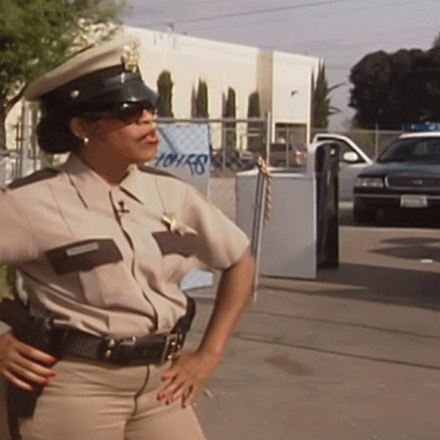A Female Police Officer Stands In Front Of A Building That Has The Word Houses On It GIF