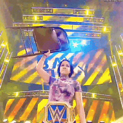 A Female Wrestler Holds A Chair Over Her Head While Wearing A W Belt GIF