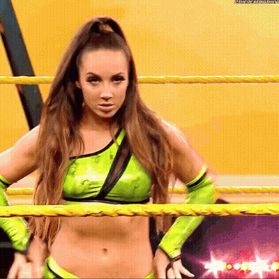 A Female Wrestler In A Green Outfit Is Standing In A Ring GIF