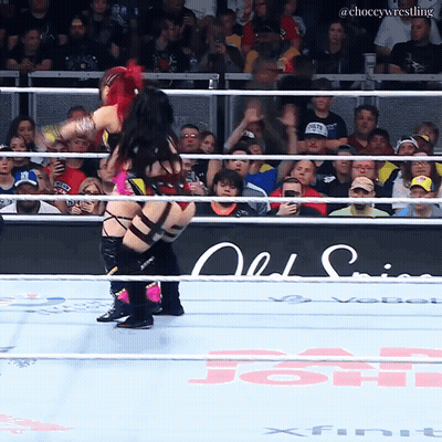 A Female Wrestler Is Being Lifted In The Air By Another Wrestler In A Wrestling Ring GIF