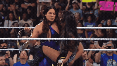 A Female Wrestler Is Carrying Another Wrestler In A Wrestling Ring While A Crowd Watches GIF
