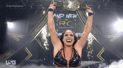 A Female Wrestler Is Holding A Championship Belt Over Her Head GIF