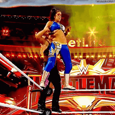 A Female Wrestler Is Standing On A Rope In A Wrestling Ring While A Man Holds Her Waist . GIF