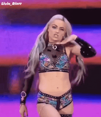 A Female Wrestler Is Standing On A Stage In A Purple And Blue Outfit . GIF