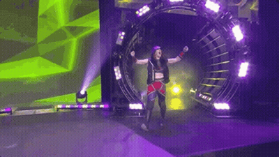 A Female Wrestler Is Walking Through A Tunnel On A Stage With Her Arms In The Air . GIF
