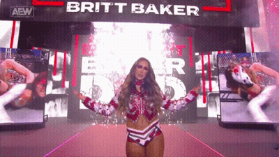 A Female Wrestler Named Britt Baker Is Standing In Front Of A Large Screen GIF