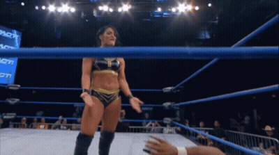 A Female Wrestler Stands In A Wrestling Ring With A Crowd Behind Her GIF