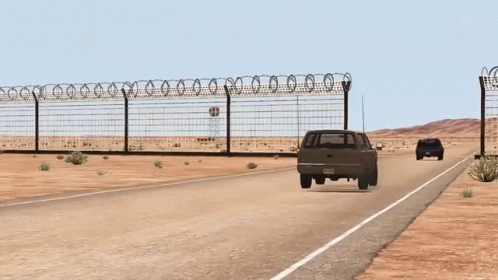 A Fence With Barbed Wire Surrounds A Desert Road GIF