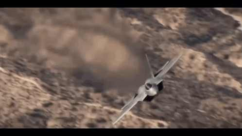 A Fighter Jet Is Flying In The Air Over A Desert Landscape . GIF