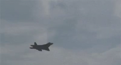 A Fighter Jet Is Flying Through A Cloudy Sky . GIF