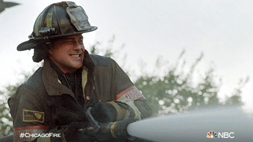 A Fireman Wearing A Helmet And A Rescue Squad Armband Is Spraying Water GIF