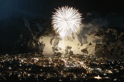 A Fireworks Display In Front Of A Snowy Mountain Over A City GIF