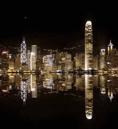 A Fireworks Display Over A City With A Reflection In The Water GIF