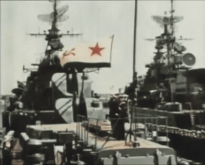 A Flag With A Red Star On It Is Flying In Front Of A Military Ship GIF