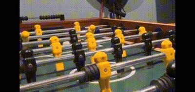 A Foosball Table With Yellow And Black Players And A Soccer Ball GIF